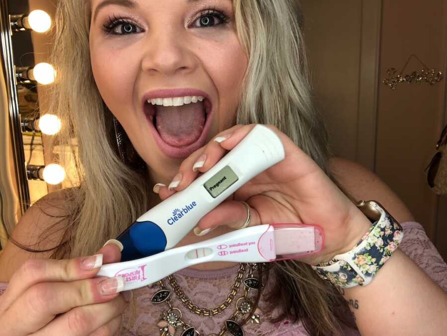 woman looks excited holding two positive pregnancy tests