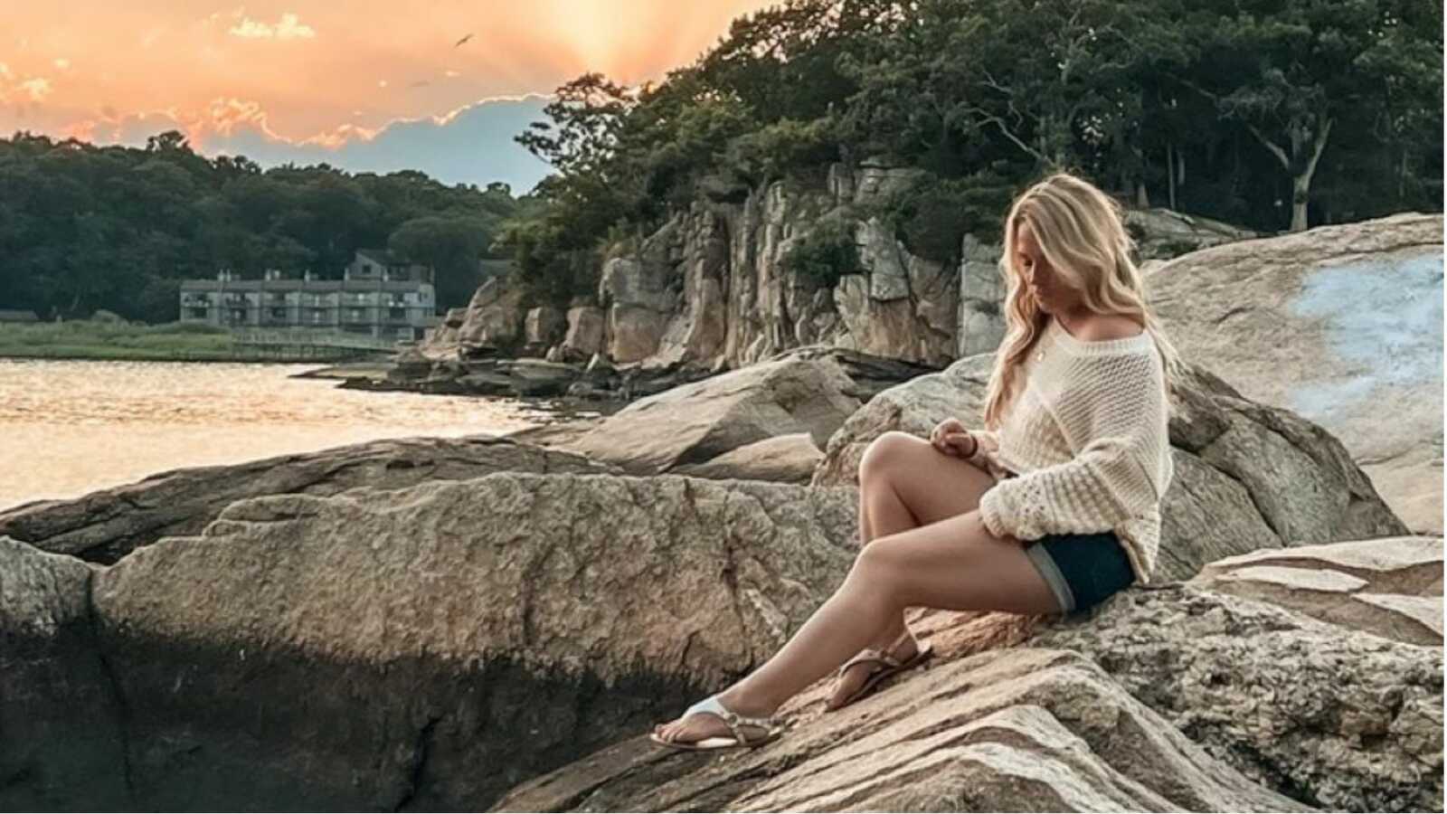 woman sitting outside on rock wearing cream colored sweater
