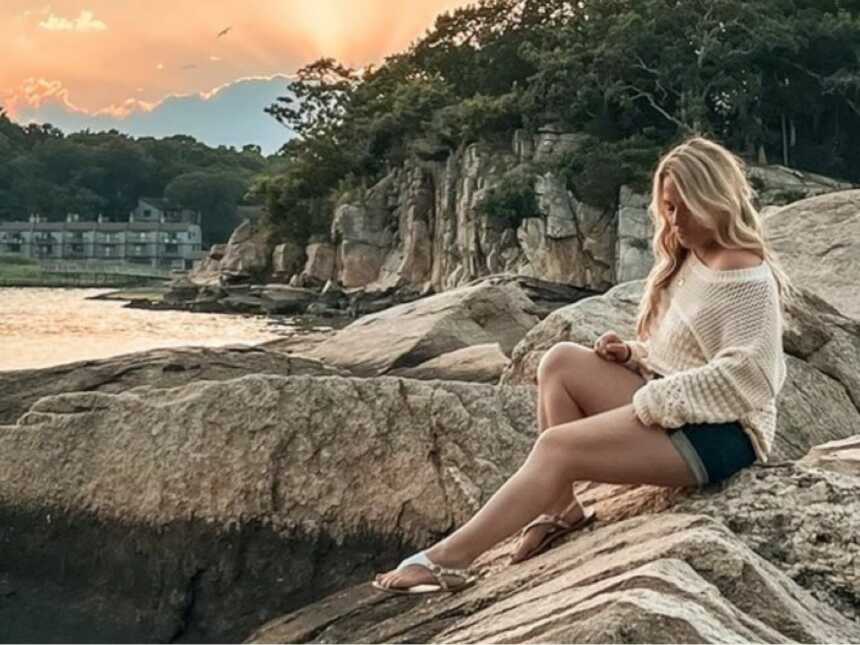 woman sitting outside on rock wearing cream colored sweater