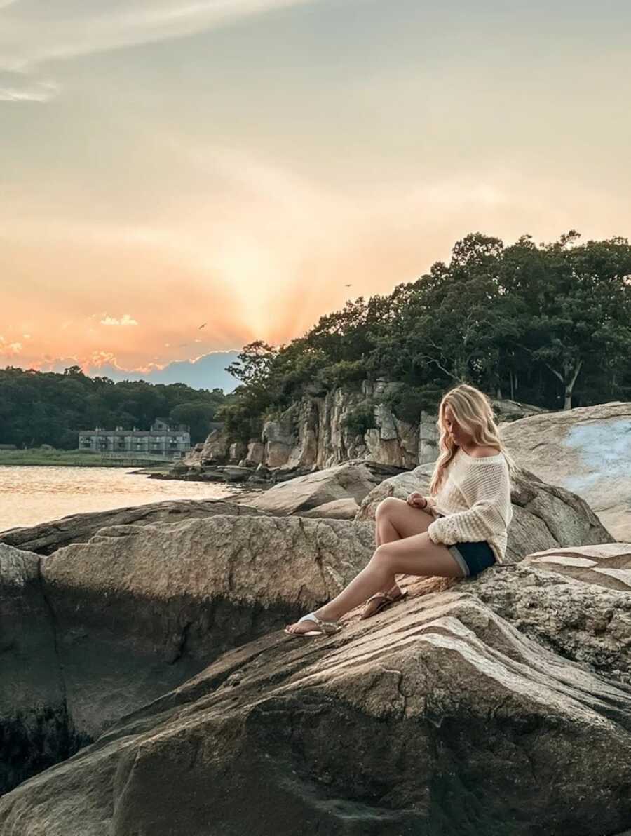 woman sitting outside on rock wearing cream colored sweater