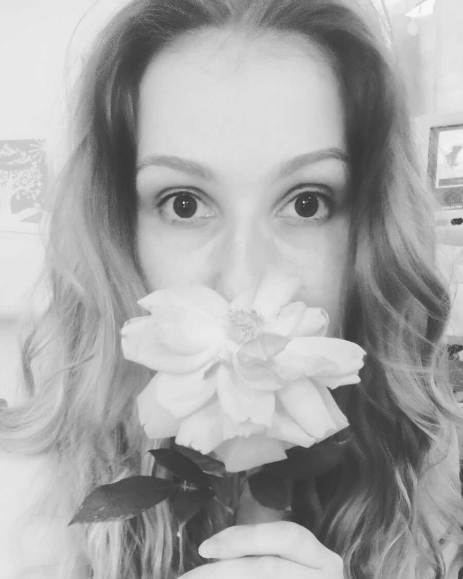 Woman holds a rose in front of her nose in black and white selfie.