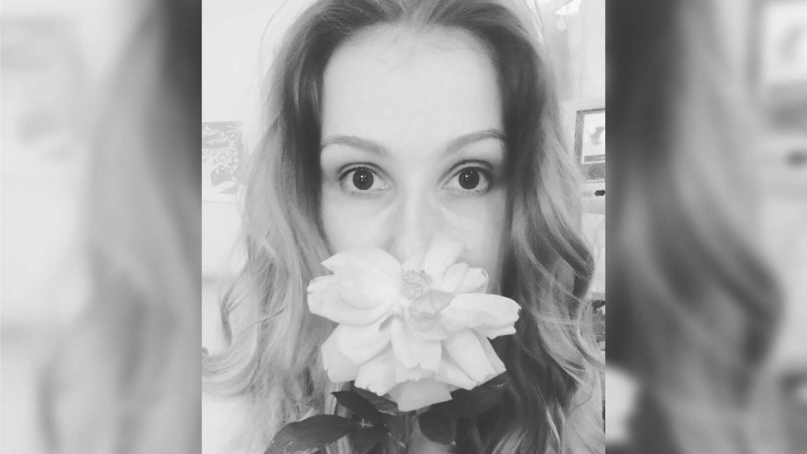 Woman holds a rose in front of her nose in black and white selfie.