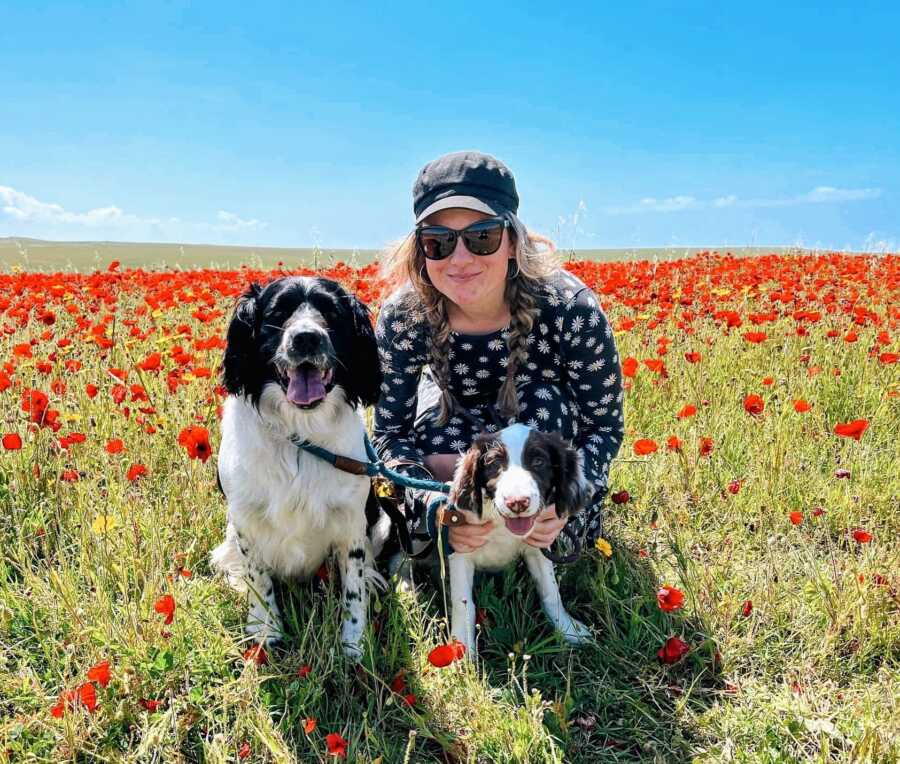 woman sitting with two dogs in a poppy field