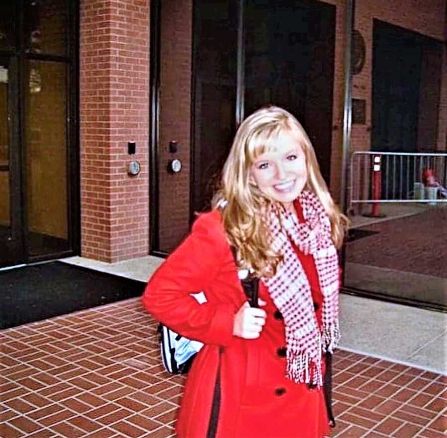 young, blonde woman wearing a long, red coat and a matching scarf outside of a building 