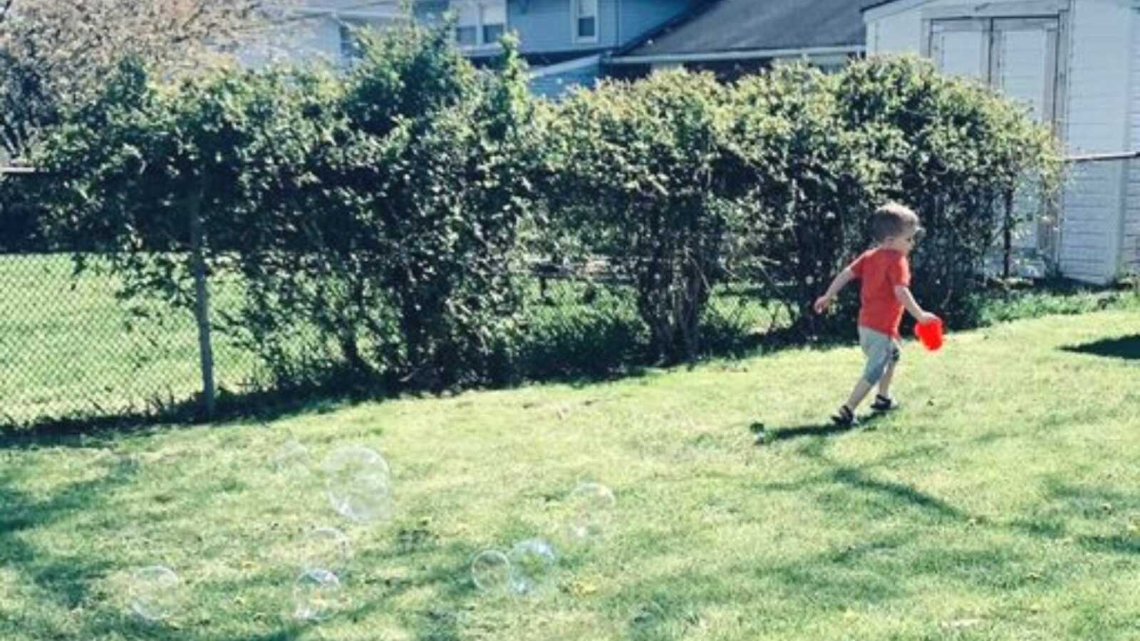 young boy playing and running outside with bubbles