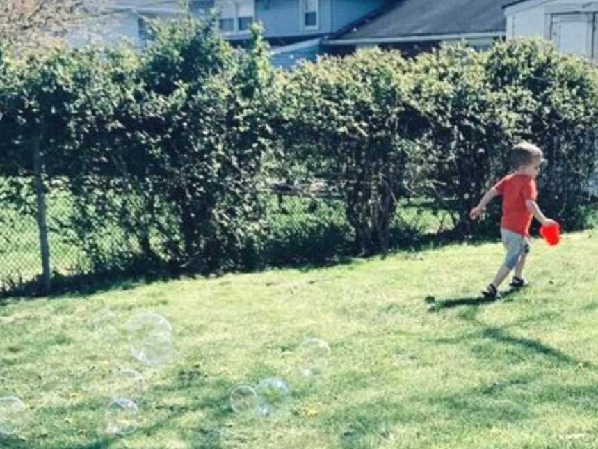 young boy playing and running outside with bubbles