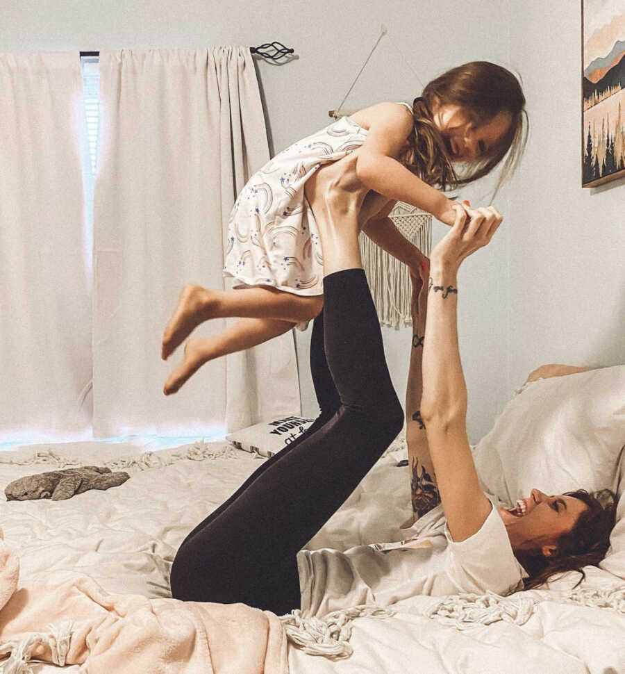 Mom lifting daughter on her arms and legs on a bed