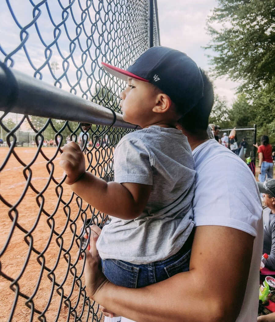Dad holding toddler son while watching a baseball game 
