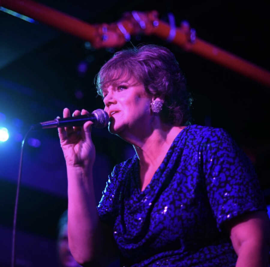 Middle-aged woman sings on stage with microphone in hand