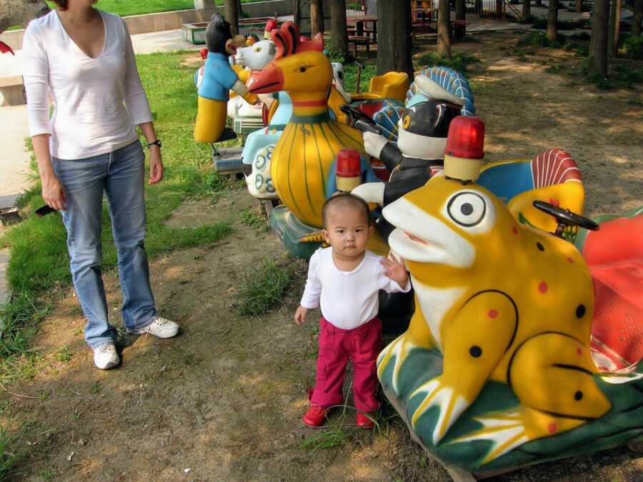 adopted daughter at play place in China with mother standing nearby