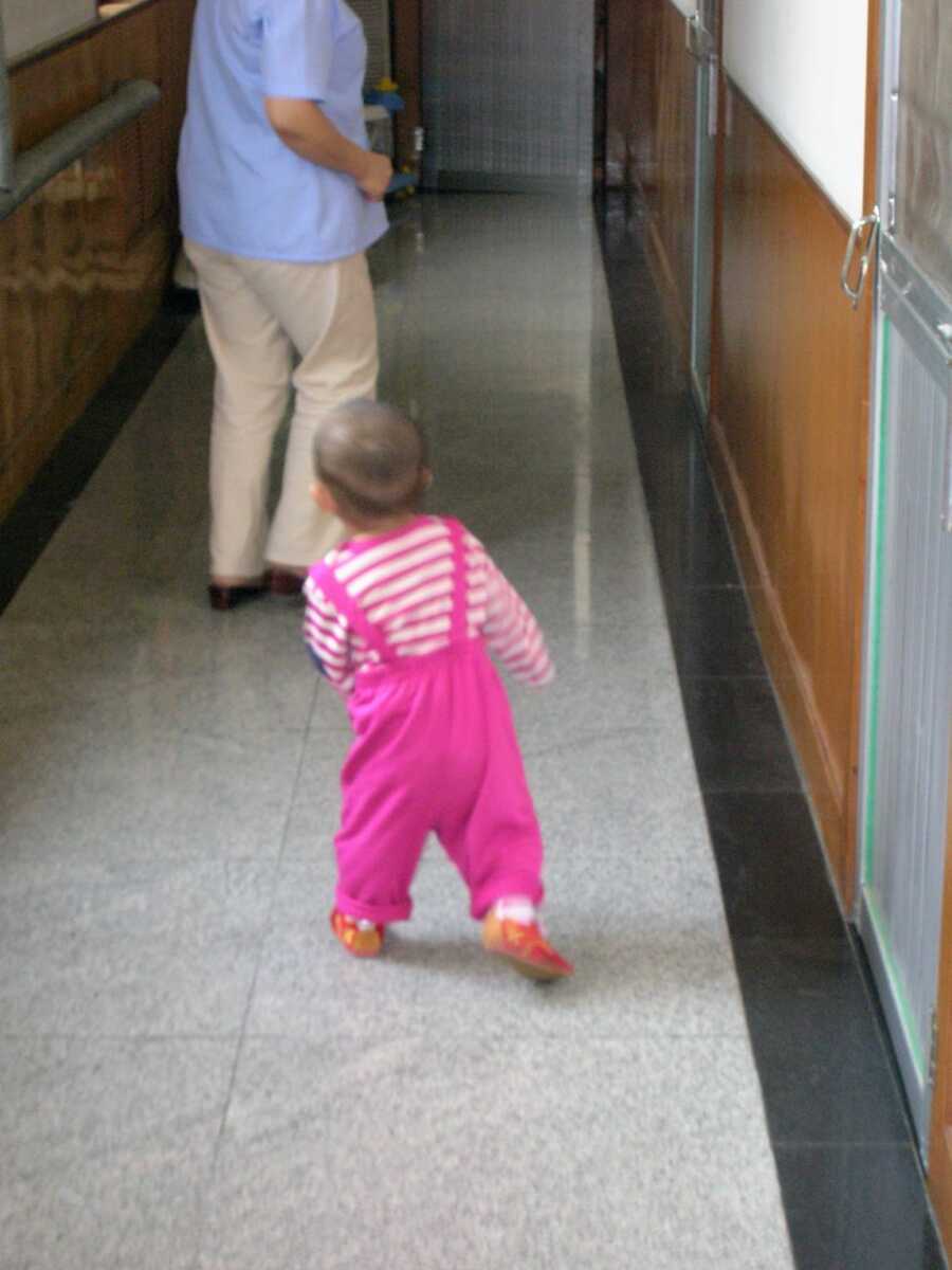 adopted daughter walking down a tile hallway in pink overalls