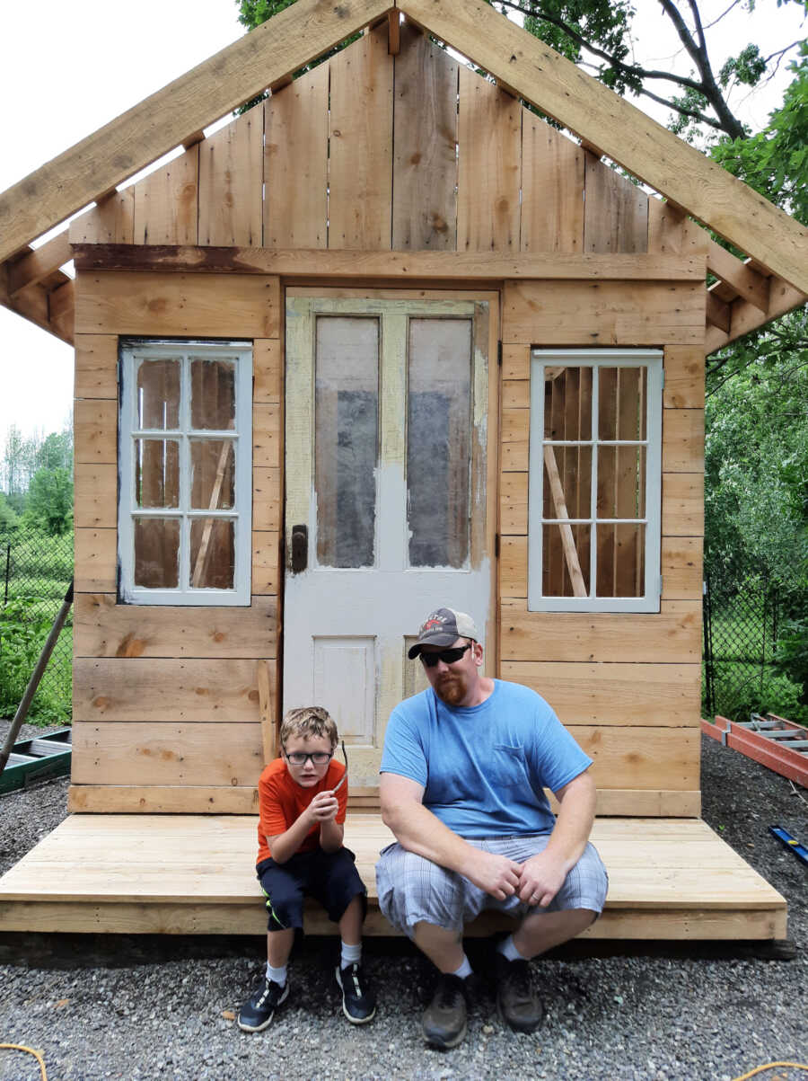 adoptive dad and son sit in front of a cabin together