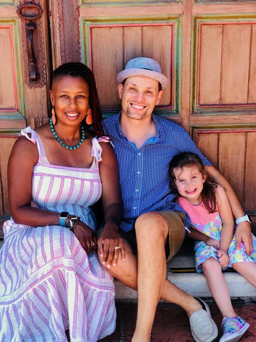 adoptive mom and dad sit against wooden wall with child