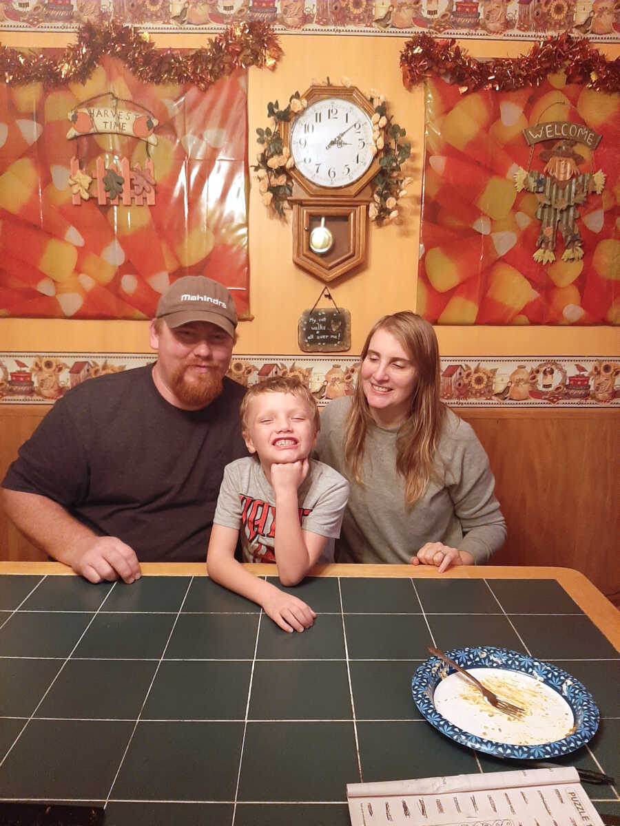 adoptive parents sit on each side of their son at the table