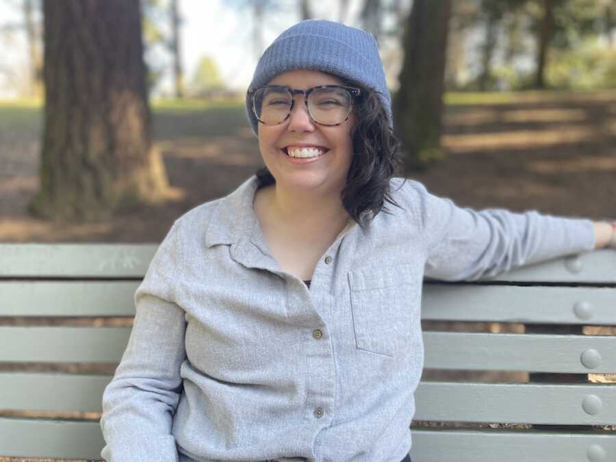 autistic, chronically ill woman wearing a beanie and sitting on a bench