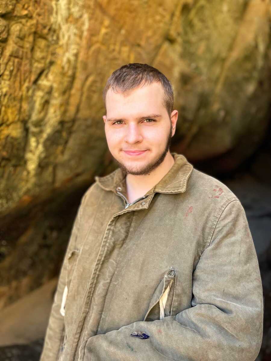 autistic man, age 20, standing outside in olive colored jacket