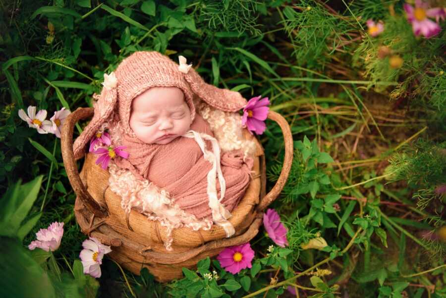 baby girl, swaddled in pink, in brown basket outside