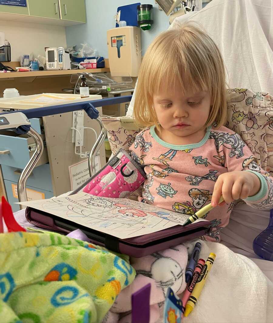 young girl colors a coloring book in a hospital bed