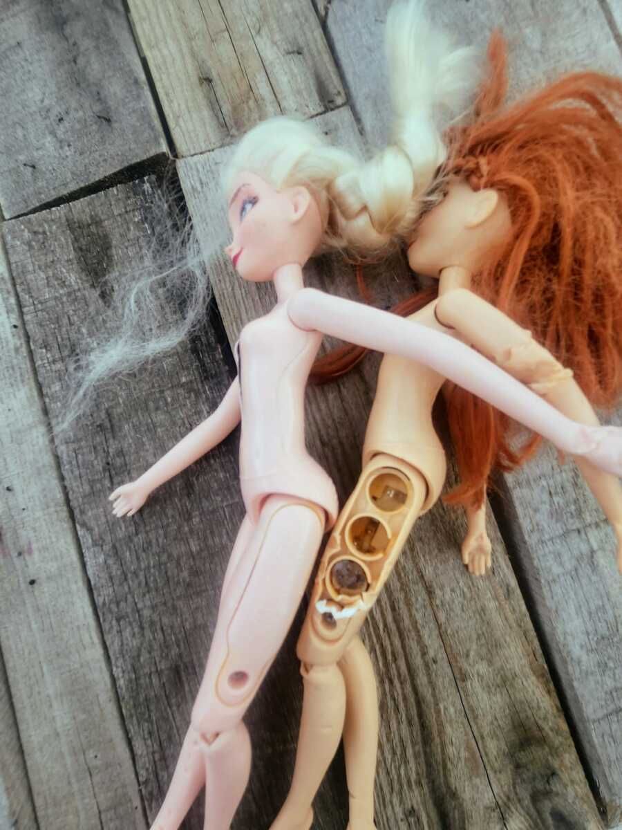 two barbie dolls beside each other showing the batteries inside leg