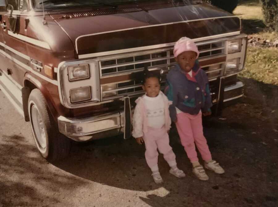 biological sisters leaning against van togehter