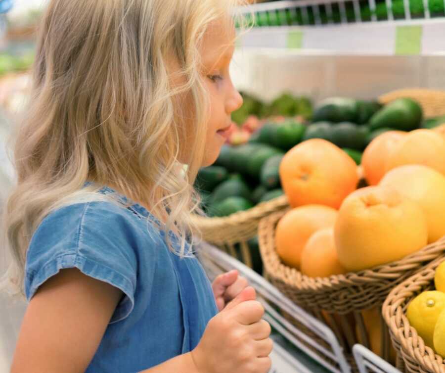 little girl analyzes produce choices at grocery store