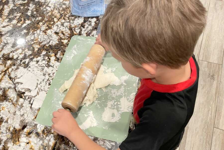 young boy using rolling pin to roll out kolaches dough