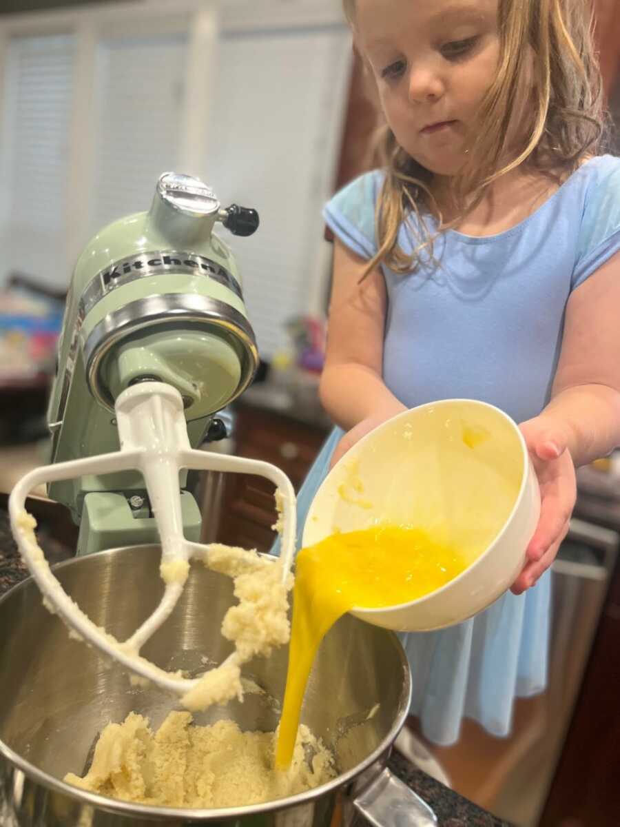 child pouring eggs into sugar cookie mix