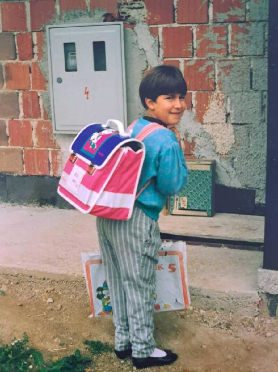 sexual abuse and eating disorder survivor as a child wearing blue shirt and backpack looking back at camera