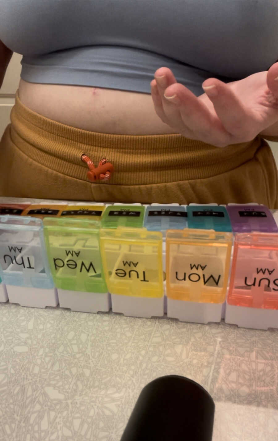 chronically ill woman standing in front of her pill box while organizing them