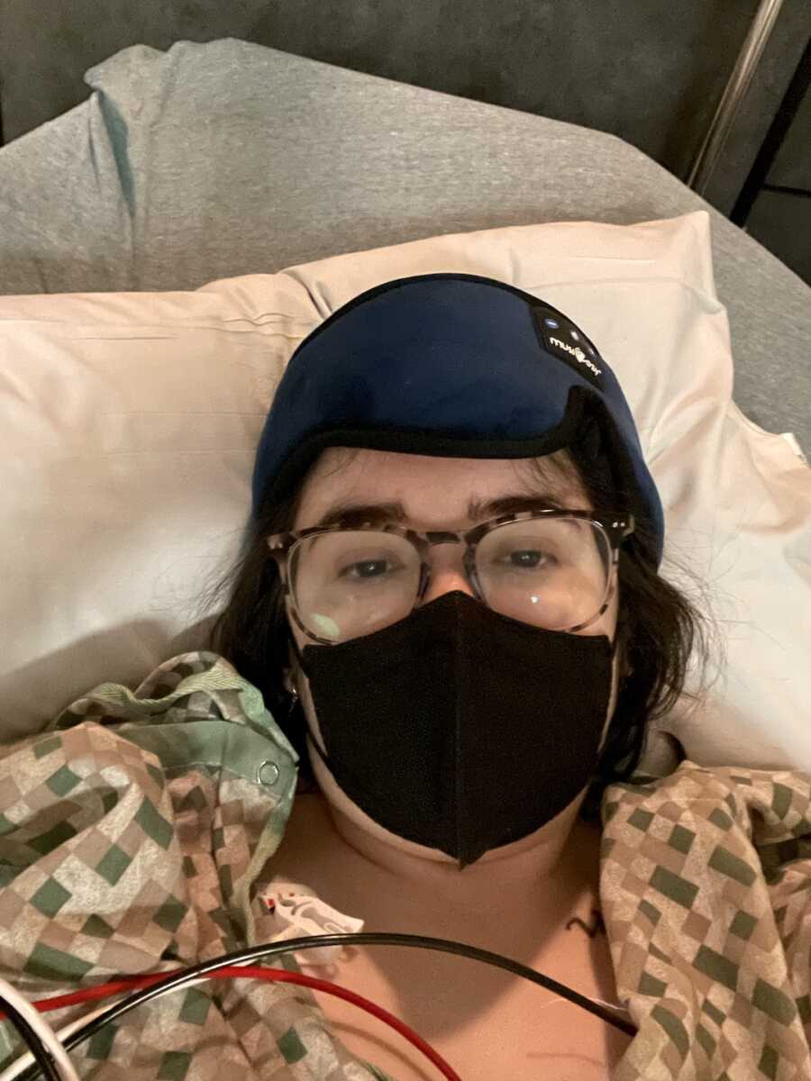 disabled, autistic, chronically ill woman laying with wires, mask, and cool pack