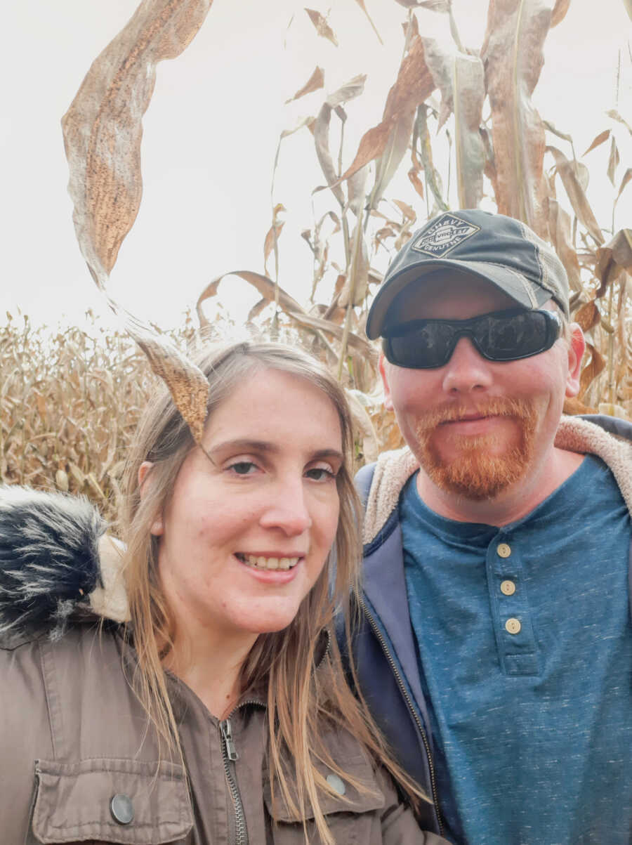 husband and wife stand together while in a corn field