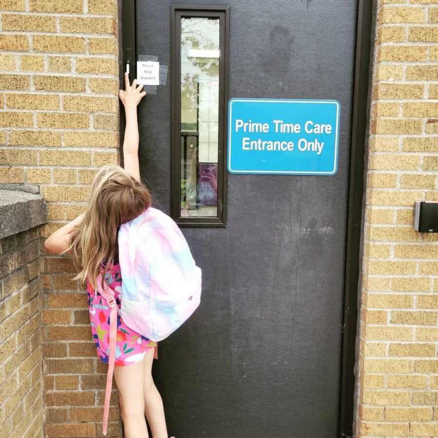 little girl reaches to ring doorbell at day care