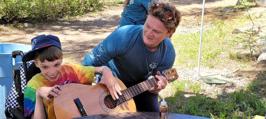 Counselor helps camper in a wheelchair play guitar 