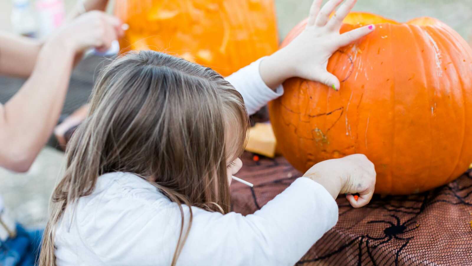 little girl carving Halloween pumpkin with family