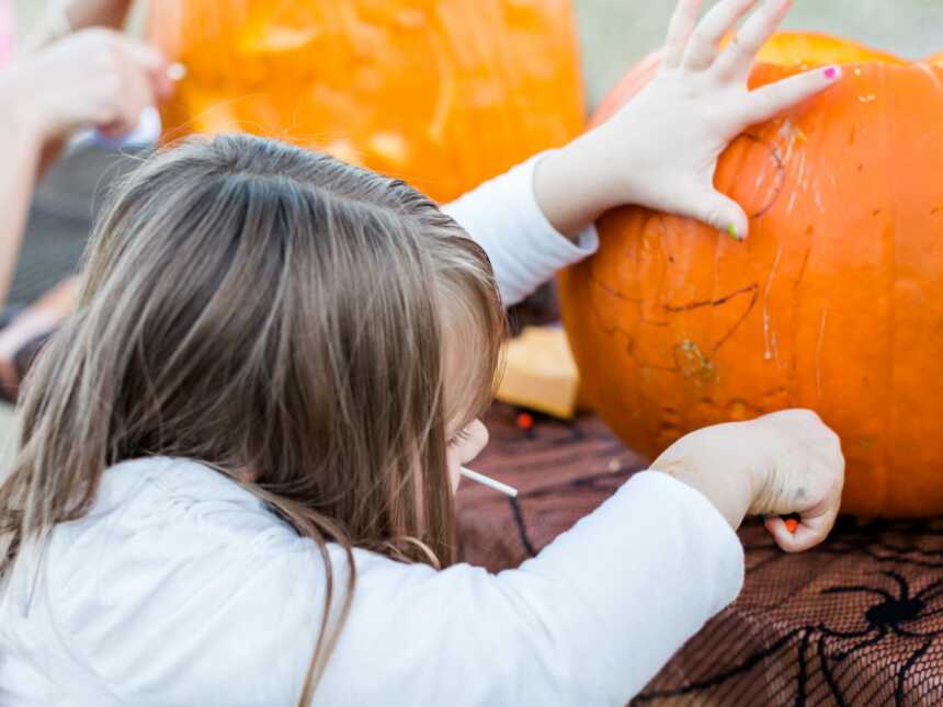 little girl carving Halloween pumpkin with family