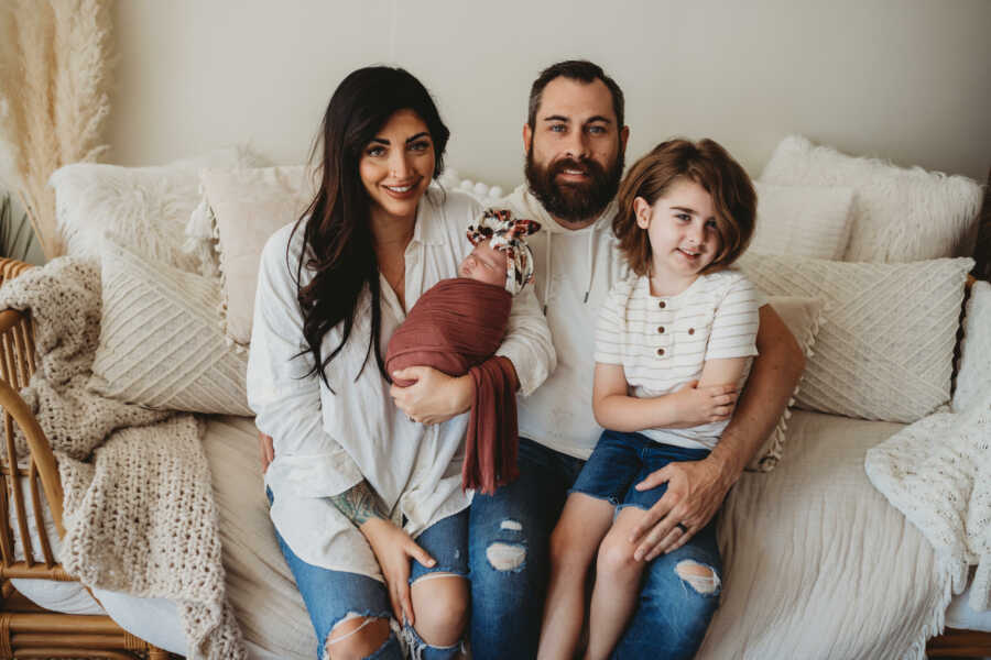 Family smiling on white couch with toddler and newborn