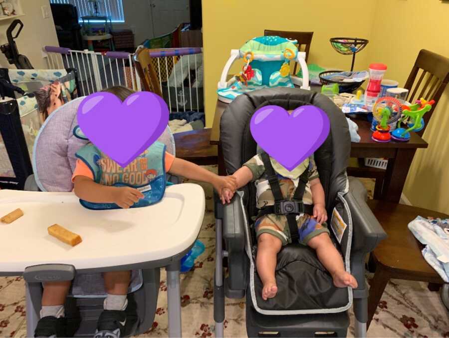 two foster children sit in high chairs and hold hands