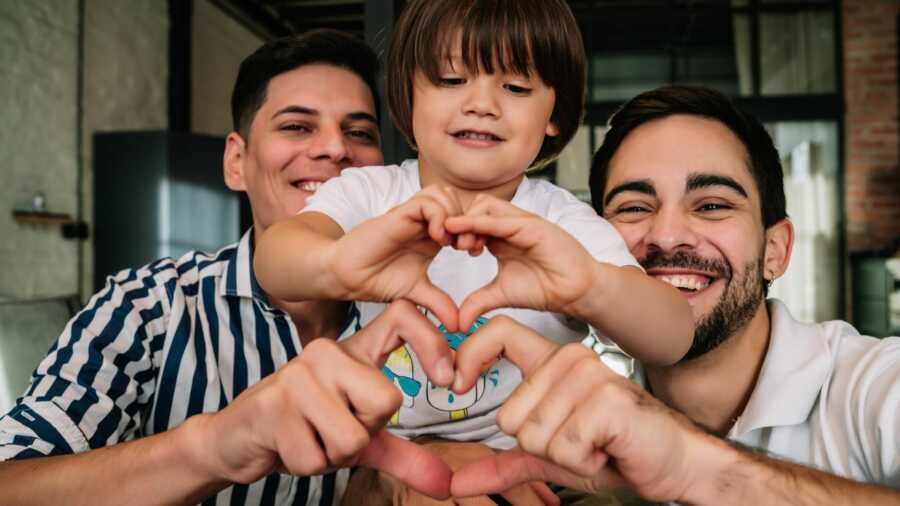 gay adoptive dads make heart shape with child