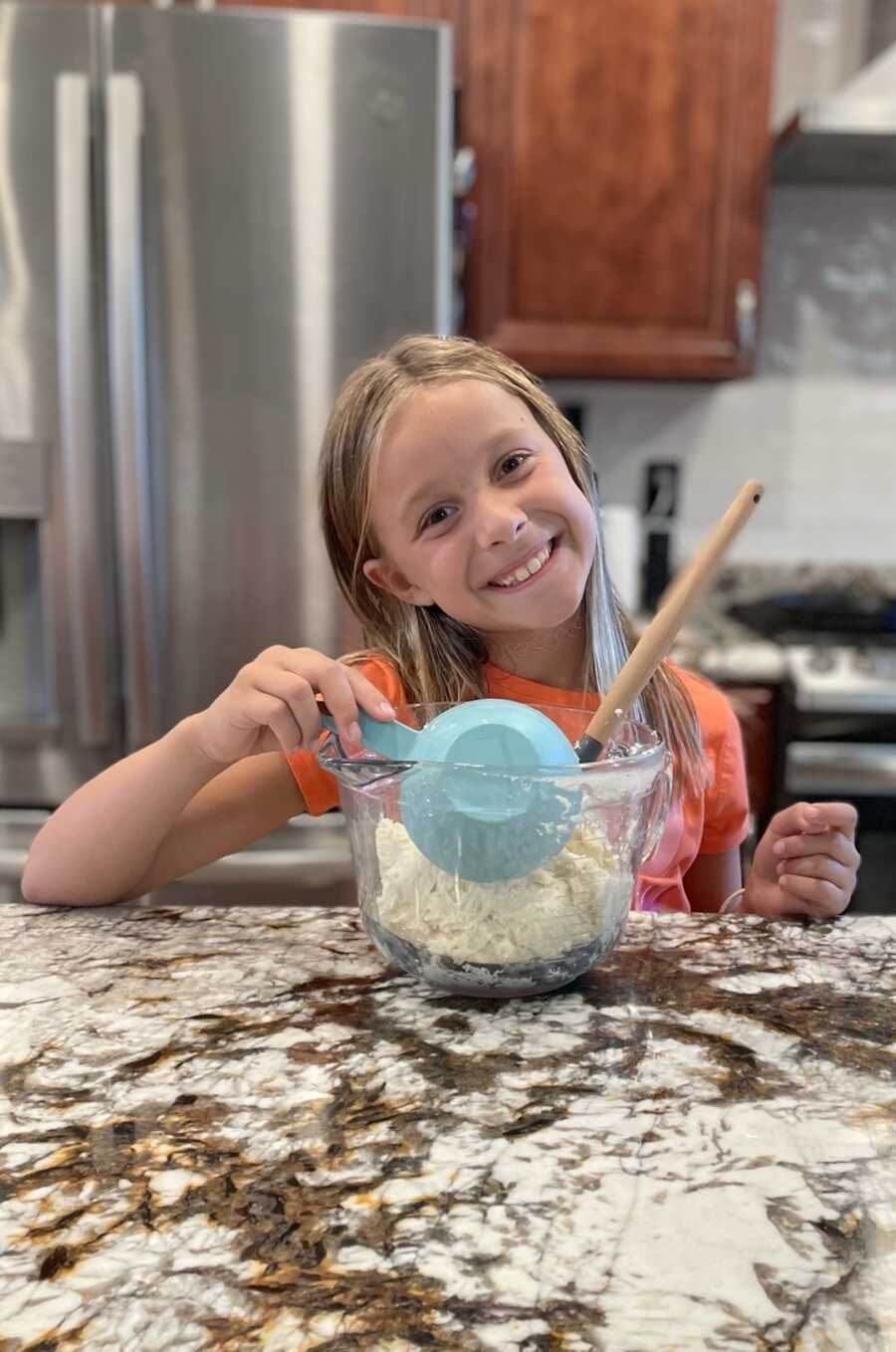 young girl using a measuring cup to mix ingredients in bowl