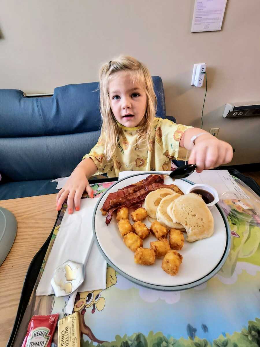 girl sits with spoon in pancakes in front of her