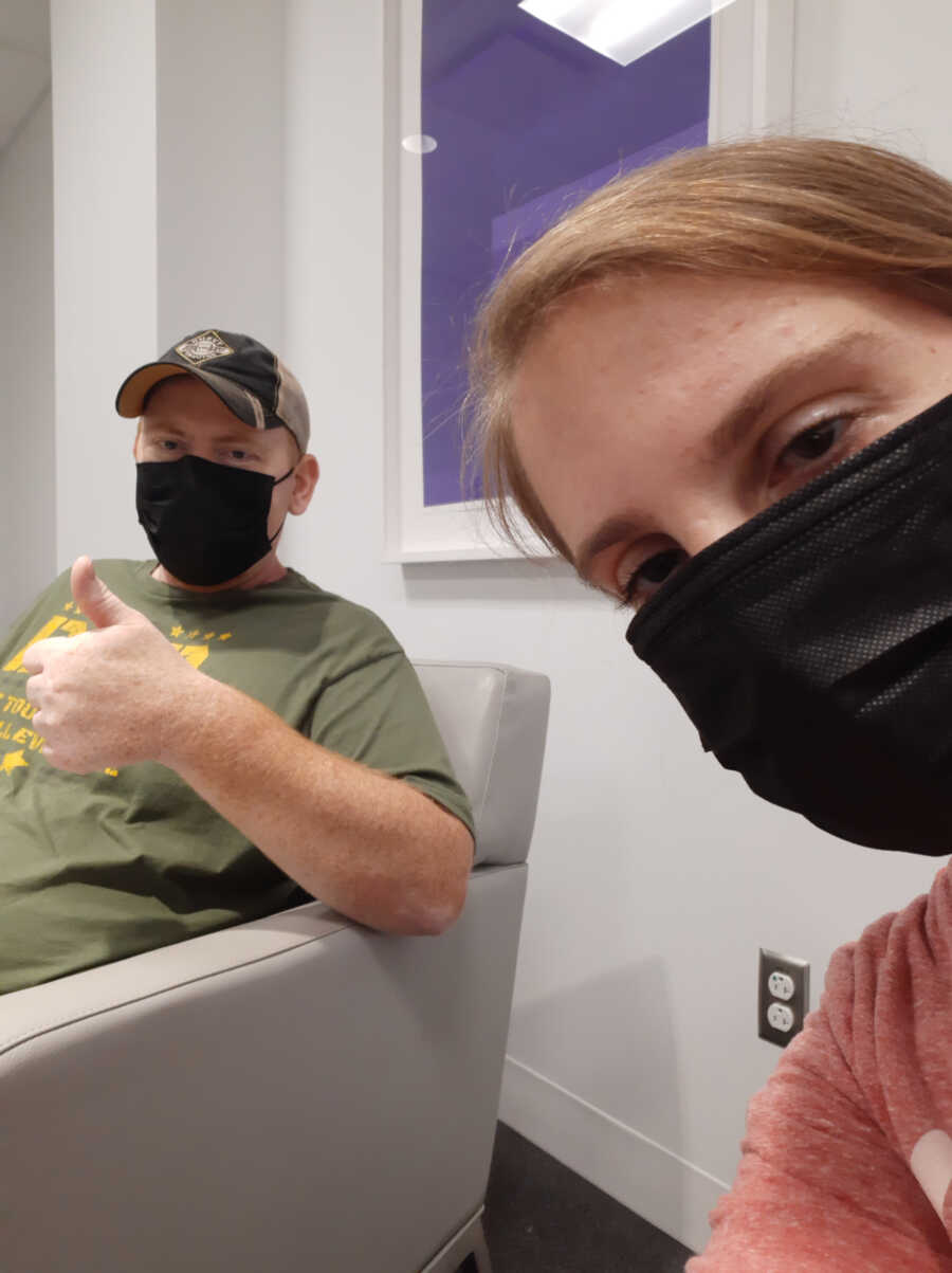 wife sits with husband while wearing masks at an appointment