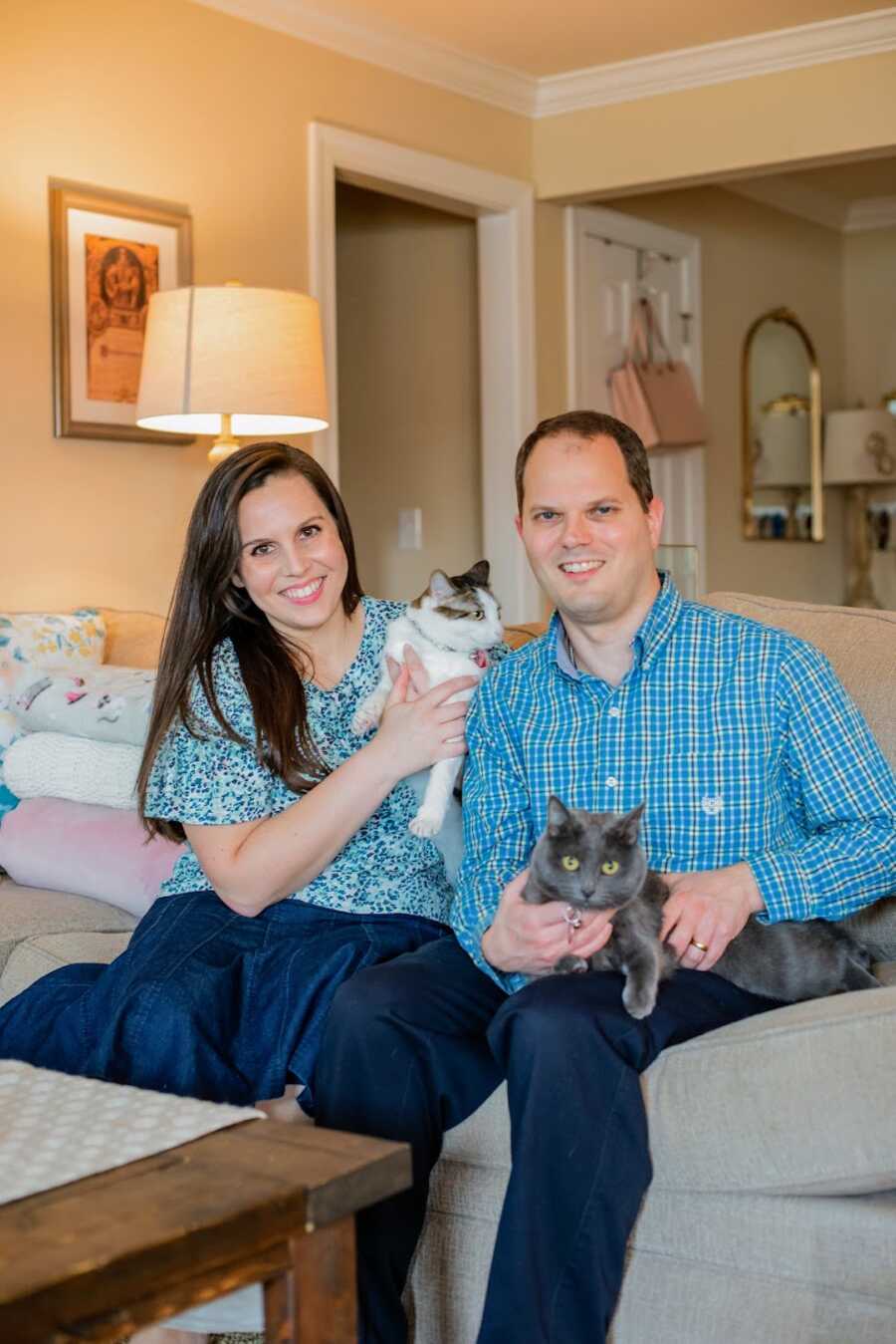 husband and wife sitting on a couch with two cats