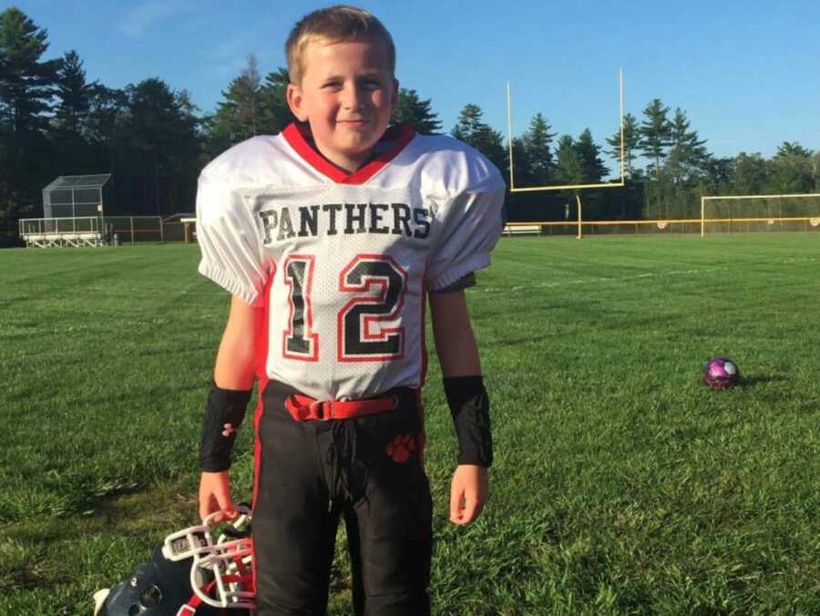 young boy wearing football jersey and gear on football field