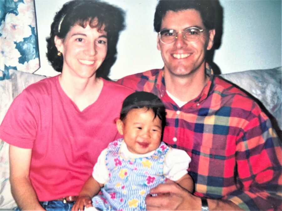 Korean baby adoptee sitting between white, adoptive parents 