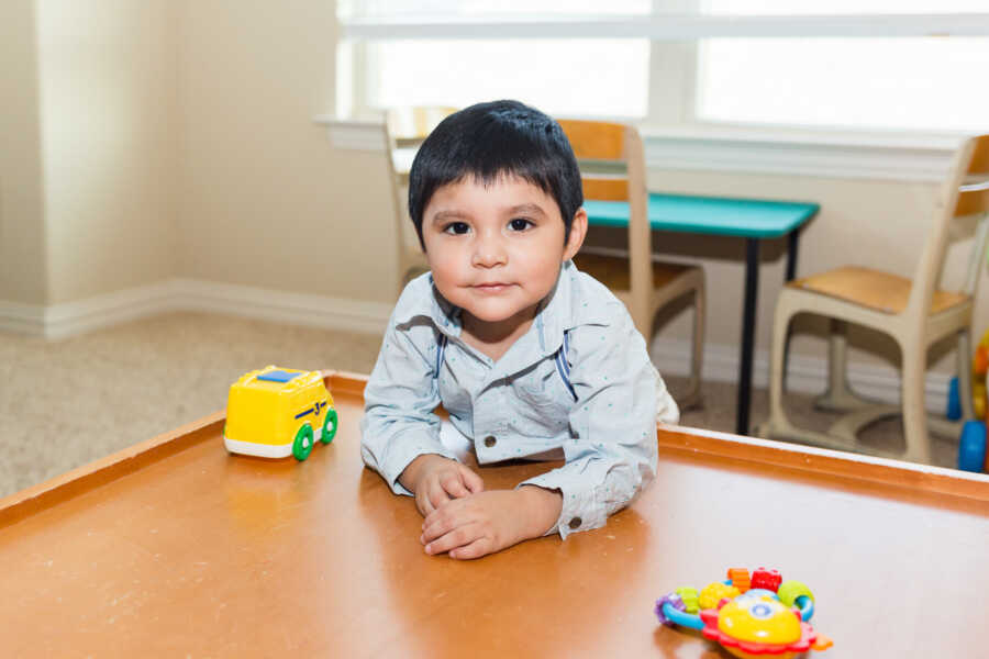 young boy leans on table with toys in front of him