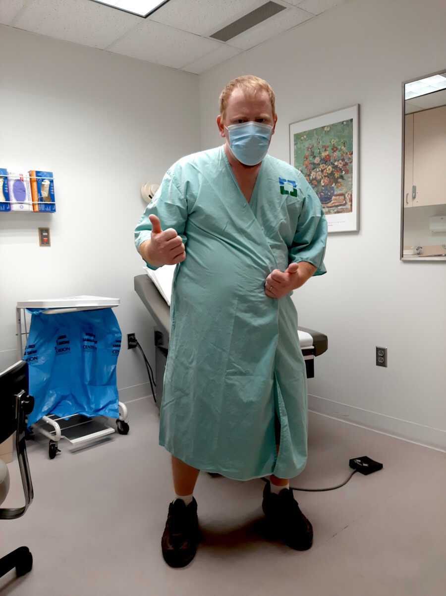 man fighting melanoma stands in hospital gown giving a thumbs up