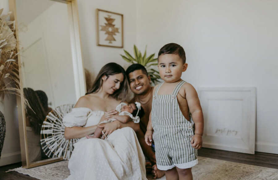 Toddler standing in front of parents holding newborn baby girl