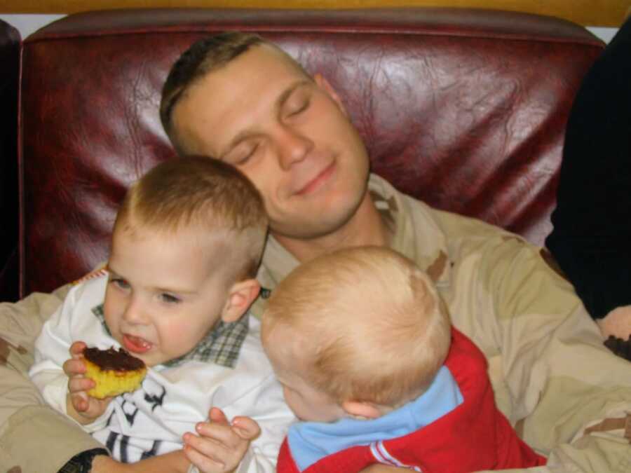 military dad holding two baby boys on couch