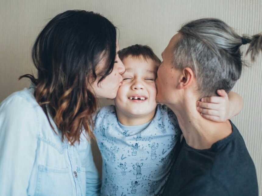 mom and dad kissing son on each cheek as he smiles