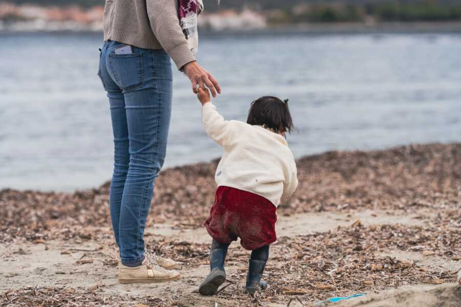 mom holding adoptive daughters hand on beach